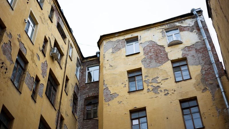 A low angle shot of a dilapidated residential building with peeling paint in an urban area.