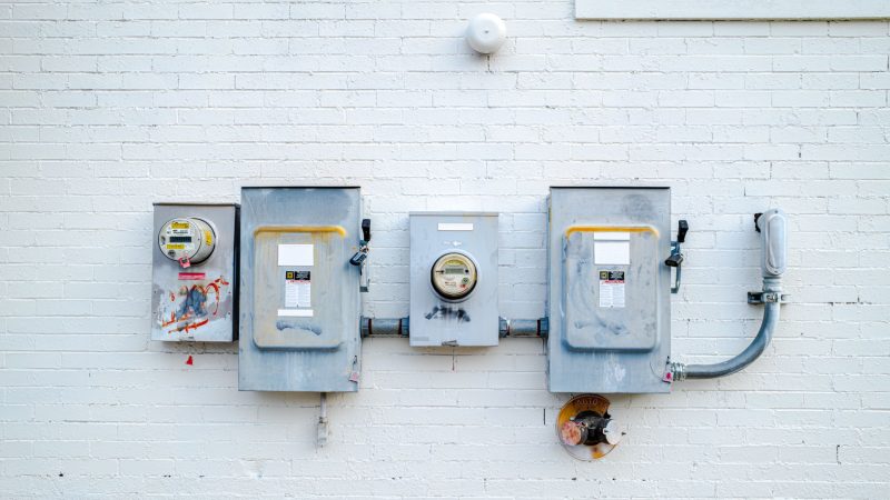 Electrical boxes and power meters mounted on a white brick wall.